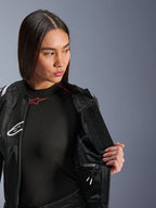 Alpinestars Stella T-SPS Air v2 Jacket, damska kurtka motocyklowa, czarna, modelka otwierająca kurtkę, aby pokazać wodoodporną wewnętrzną komorę, z panelami z siatki technicznej i wytrzymałą konstrukcją tekstylną