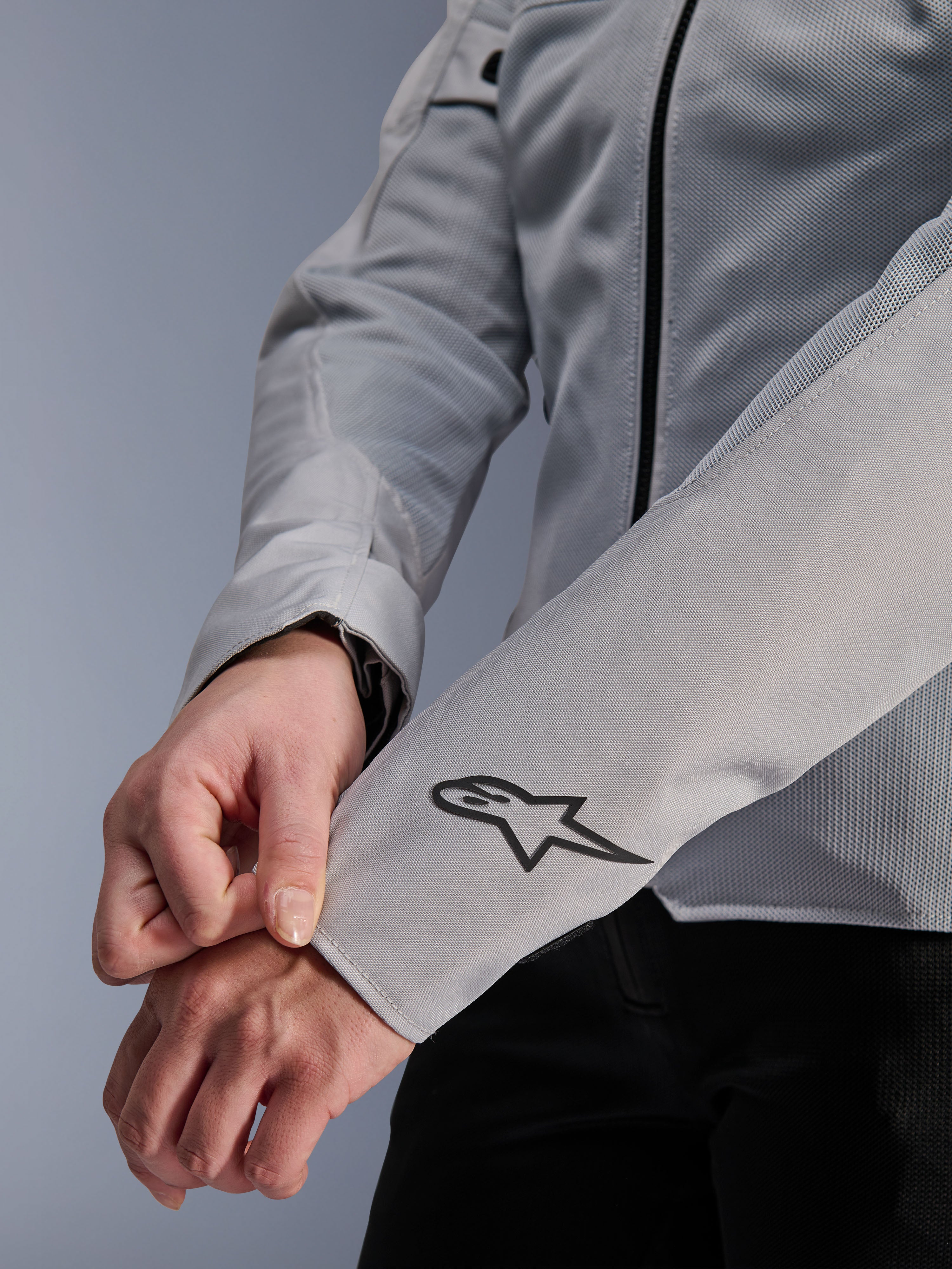 Zbliżenie na kurtkę Alpinestars Stella C-1 Air w kolorze srebrnym, z konstrukcją z technicznej siatki i czarnym logo Alpinestars na lewym rękawie, miejska kurtka motocyklowa dla kobiet z odblaskowym brandingiem.