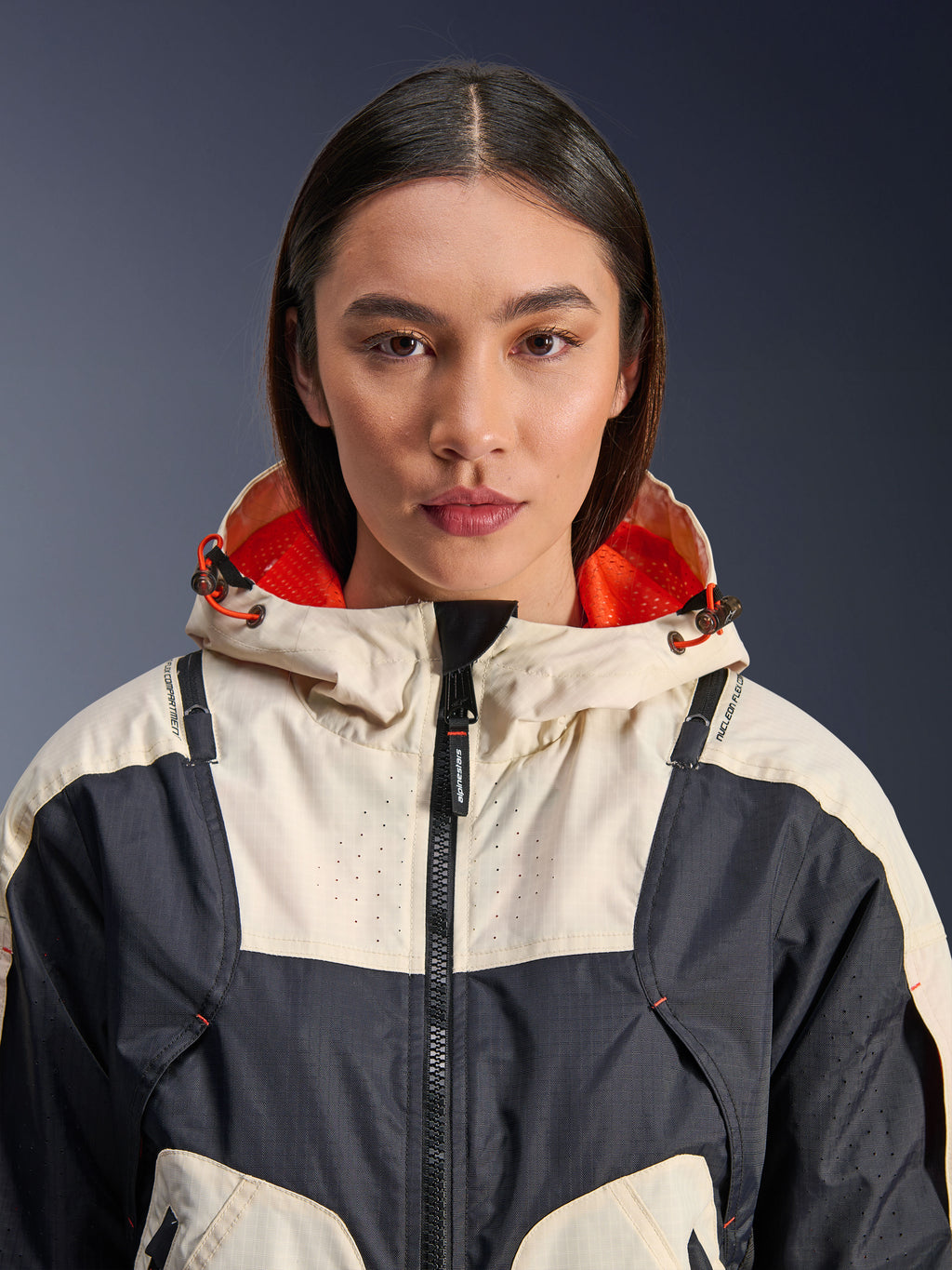 Alpinestars Molly Air Jacket, damska tekstylna kurtka motocyklowa, Black Almond, widok z bliska od przodu na modelkę w kurtce o kremowo-czarnej panelowej konstrukcji, kaptur z jaskrawopomarańczową podszewką z siatki i laserowe perforacje na klatce piersiowej