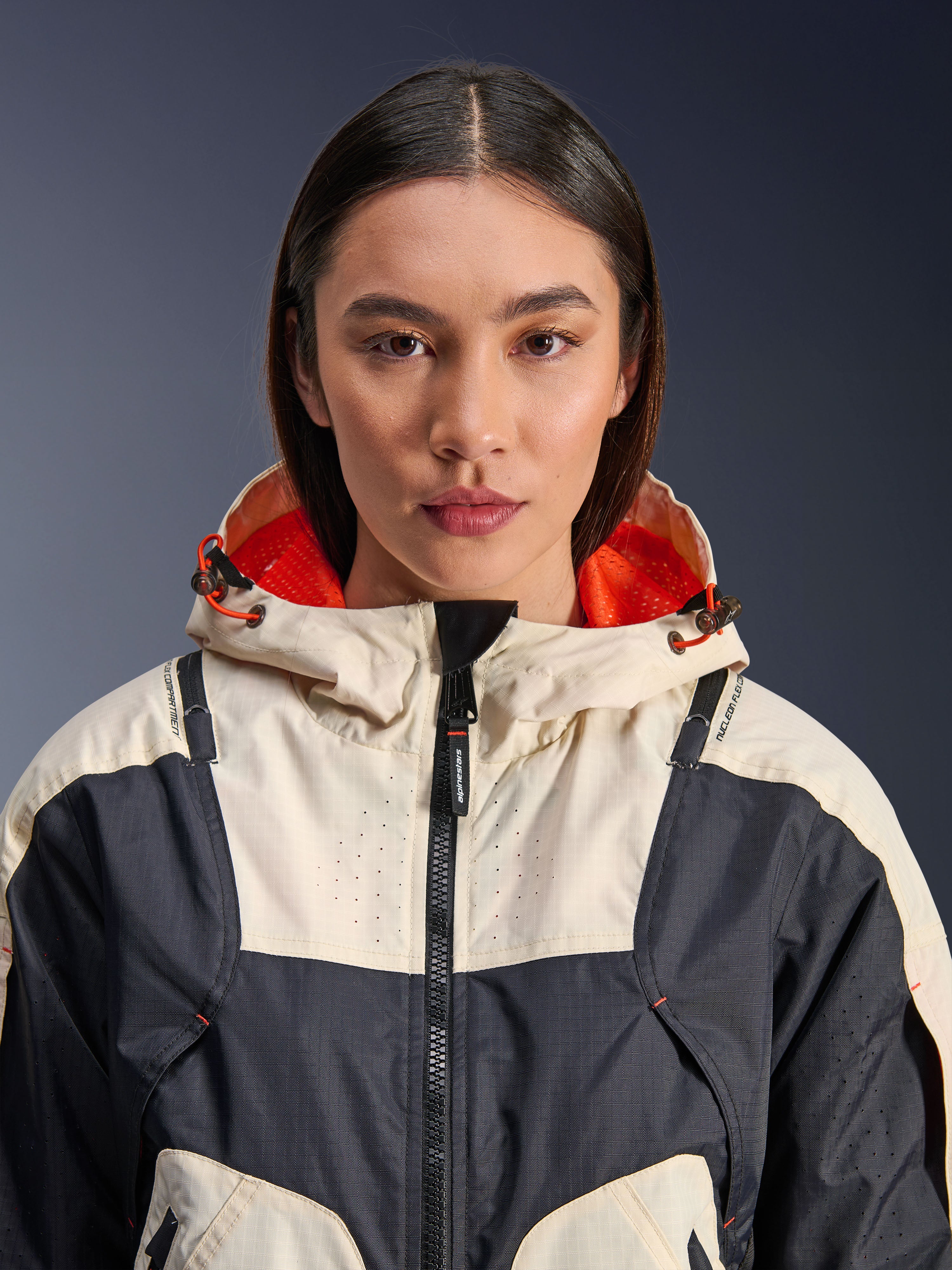 Alpinestars Molly Air Jacket, damska tekstylna kurtka motocyklowa, Black Almond, widok z bliska od przodu na modelkę w kurtce o kremowo-czarnej panelowej konstrukcji, kaptur z jaskrawopomarańczową podszewką z siatki i laserowe perforacje na klatce piersiowej