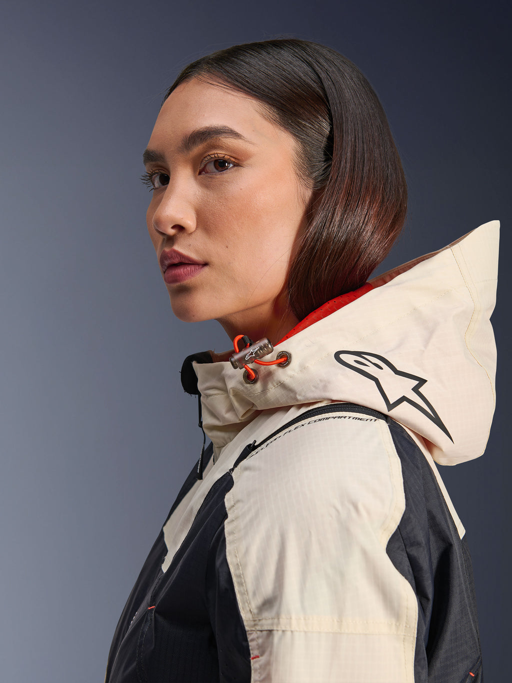 Alpinestars Molly Air Jacket, Black Almond, współczesna miejska kurtka motocyklowa, widok z profilu na modelkę w kapturze z logo Alpinestars i pomarańczowymi akcentami ściągacza, tekstura materiału ripstop