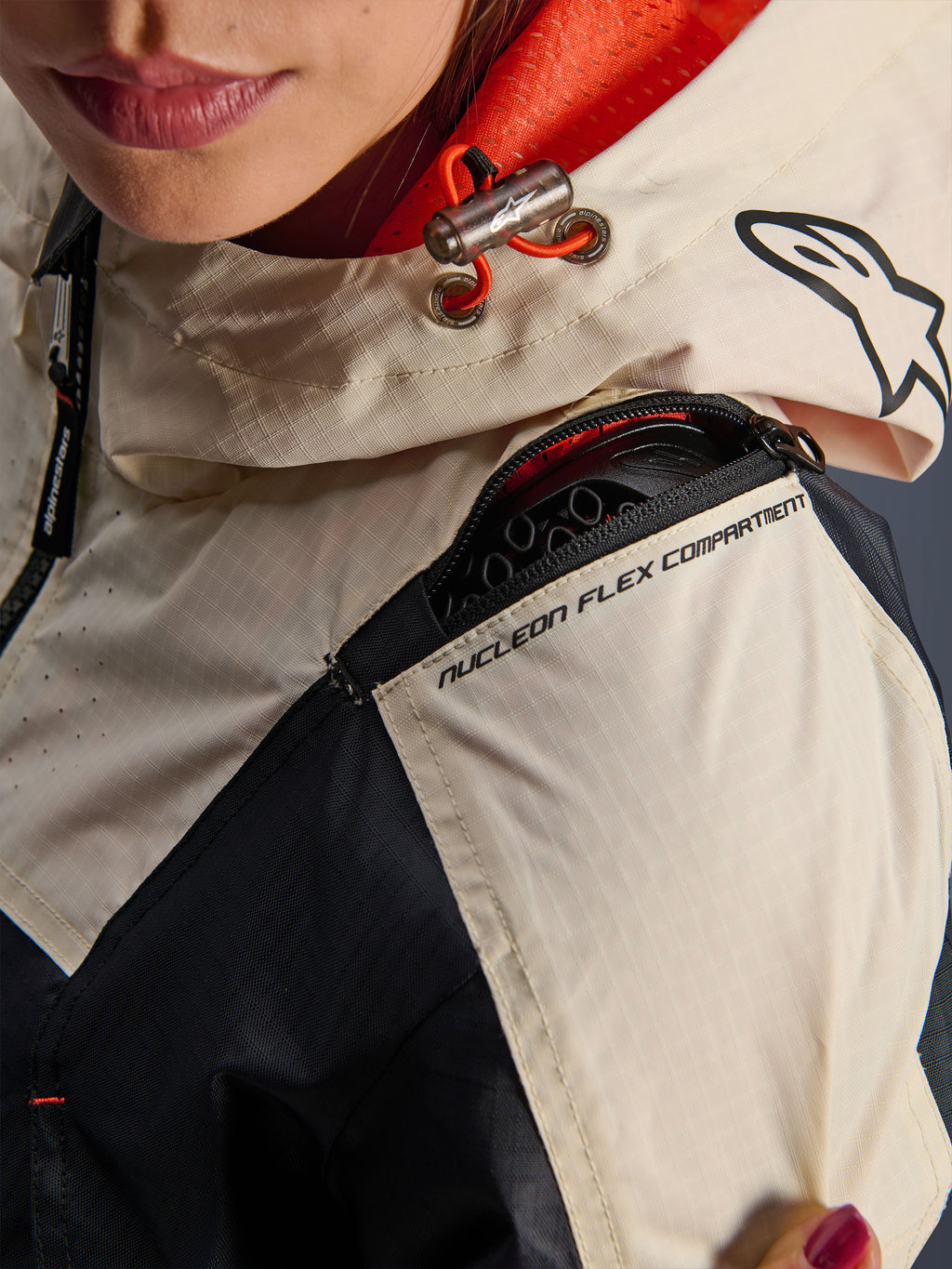Kurtka Alpinestars Molly Air, damska kurtka motocyklowa, Black Almond, zbliżenie na ramię pokazujące zamek błyskawiczny przegrody Nucleon Flex Compartment, materiał ripstop oraz pomarańczową podszewkę z siatki wewnątrz kaptura