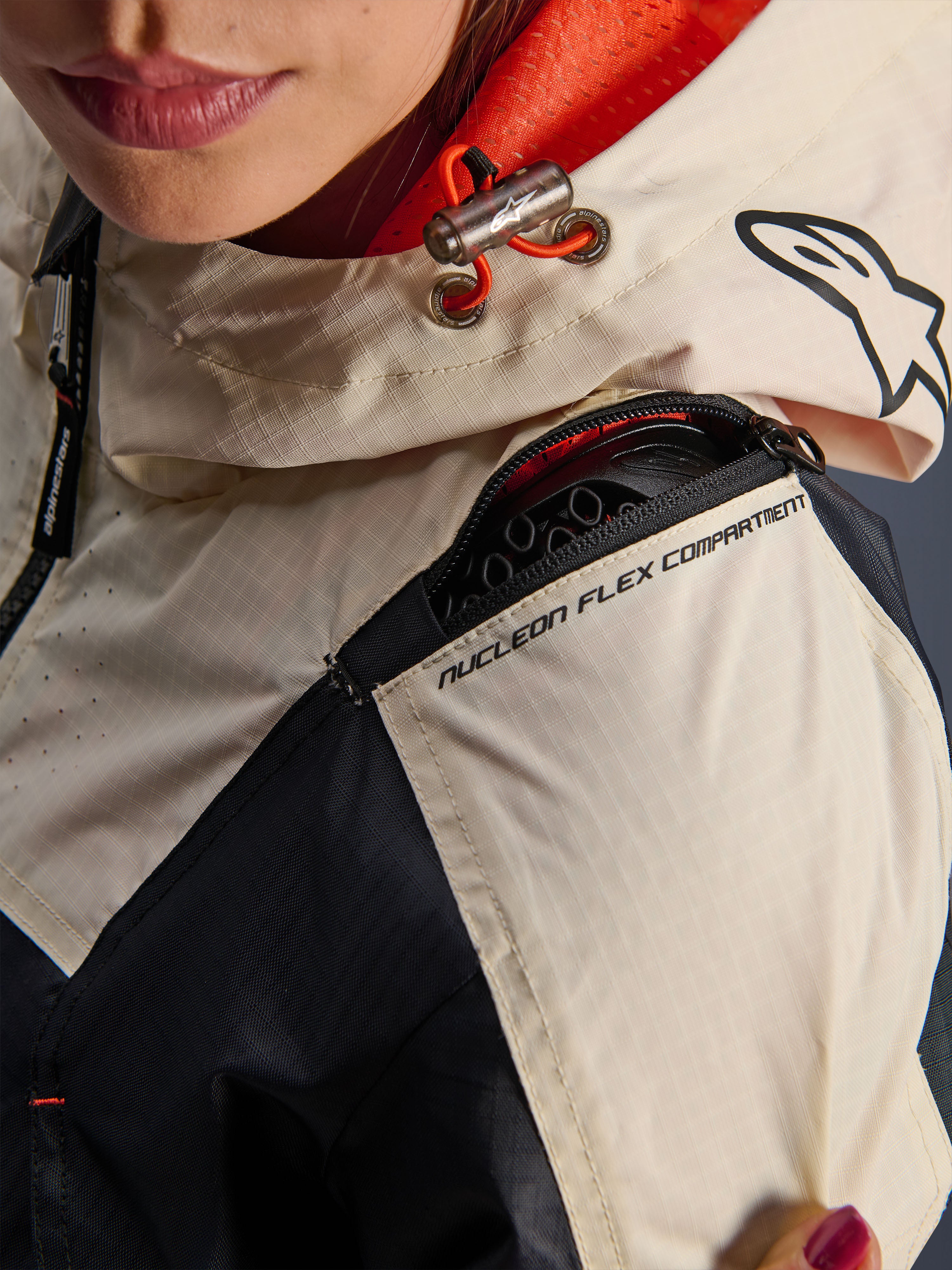 Kurtka Alpinestars Molly Air, damska kurtka motocyklowa, Black Almond, zbliżenie na ramię pokazujące zamek błyskawiczny przegrody Nucleon Flex Compartment, materiał ripstop oraz pomarańczową podszewkę z siatki wewnątrz kaptura