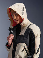Alpinestars Molly Air Jacket w kolorze Black Almond, noszona przez modelkę z założonym kapturem, z kremowo-czarnymi panelami kolorystycznymi, wyrazistą pomarańczową podszewką z siateczki i technicznymi miejskimi elementami designu, w tym logo z gwiazdą i detalami z zamkami.