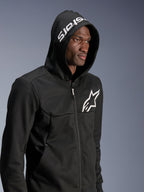 Alpinestars Chrome V2 Sport Hoodie, czarna miejska bluza motocyklowa noszona przez modela z założonym kapturem, białe logo gwiazdy na klatce piersiowej i biały napis stars na kapturze, konstrukcja z technicznego polaru, casualowy motocyklowy streetwear