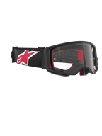 Gogle Alpinestars Supertech Corp, gogle motocrossowe, czarno-czerwone z przezroczystą szybką, widok pod kątem prezentujący przezroczystą soczewkę i czarną oprawkę, czerwona wyściółka wewnętrzna, czarny pasek z dużym czerwono-białym logo Alpinestars, profesjonalna ochrona oczu off-road