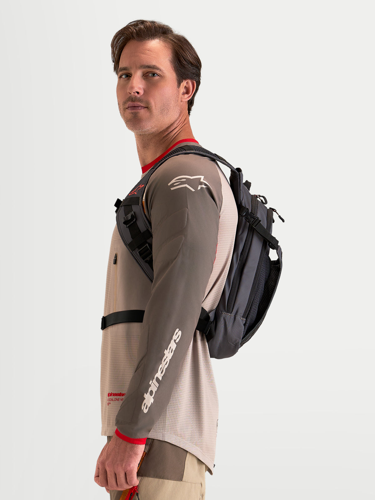 Alpinestars Plecak AT-9, plecak motocyklowy motocross w kolorze brązowym i ciemnoszarym, na męskim modelu prezentującym profil szelek bocznych i lekką konstrukcję tekstylną