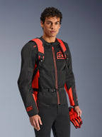 Plecak Alpinestars MM93 AMP3, jaskrawoczerwony i czarny, noszony przez modela z pasującą czarno-czerwoną kurtką motocyklową i rękawicami MM93, widok z przodu podkreślający regulowane paski naramienne i klamrę piersiową, techniczny sprzęt inspirowany wyścigami