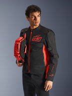 Alpinestars MM93 Waist Bag, torba na pas w kolorze czerwonym fluo i czarnym, trzymana przez modela w pasującej czarno-czerwonej kurtce motocyklowej, wyposażona w wiele przegród na zamek i branding Marca Marqueza, praktyczne wyposażenie do jazdy sportowej