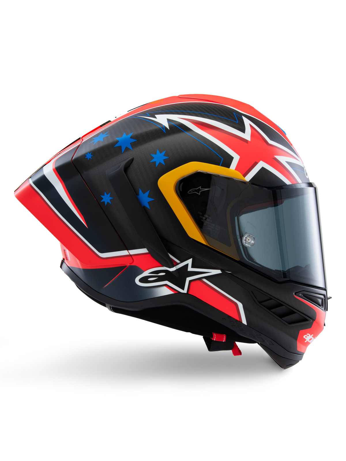 Kask Alpinestars Supertech R10 Miller Limited Edition, integralny kask wyścigowy, matowe włókno węglowe z czerwono-biało-niebieską grafiką, niebieskie akcenty w gwiazdy i żółte wykończenie wizjera, aerodynamiczny profil z przyciemnianą szybką, wysokiej klasy motocyklowy sprzęt ochronny
