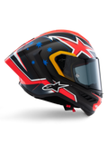 Kask Alpinestars Supertech R10 Miller Limited Edition, integralny kask wyścigowy, matowe włókno węglowe z czerwono-biało-niebieską grafiką, niebieskie akcenty w gwiazdy i żółte wykończenie wizjera, aerodynamiczny profil z przyciemnianą szybką, wysokiej klasy motocyklowy sprzęt ochronny