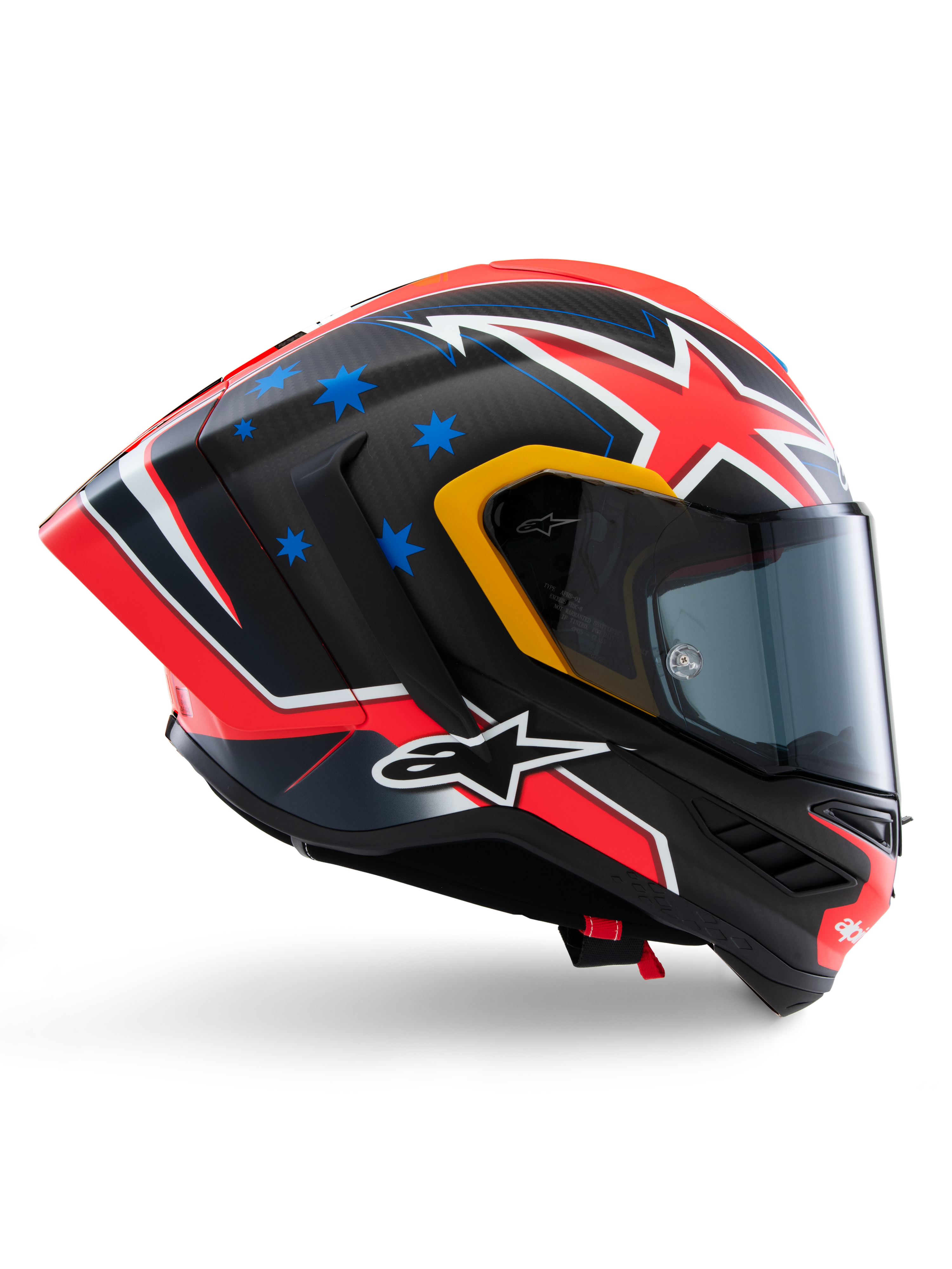 Kask Alpinestars Supertech R10 Miller Limited Edition, integralny kask wyścigowy, matowe włókno węglowe z czerwono-biało-niebieską grafiką, niebieskie akcenty w gwiazdy i żółte wykończenie wizjera, aerodynamiczny profil z przyciemnianą szybką, wysokiej klasy motocyklowy sprzęt ochronny