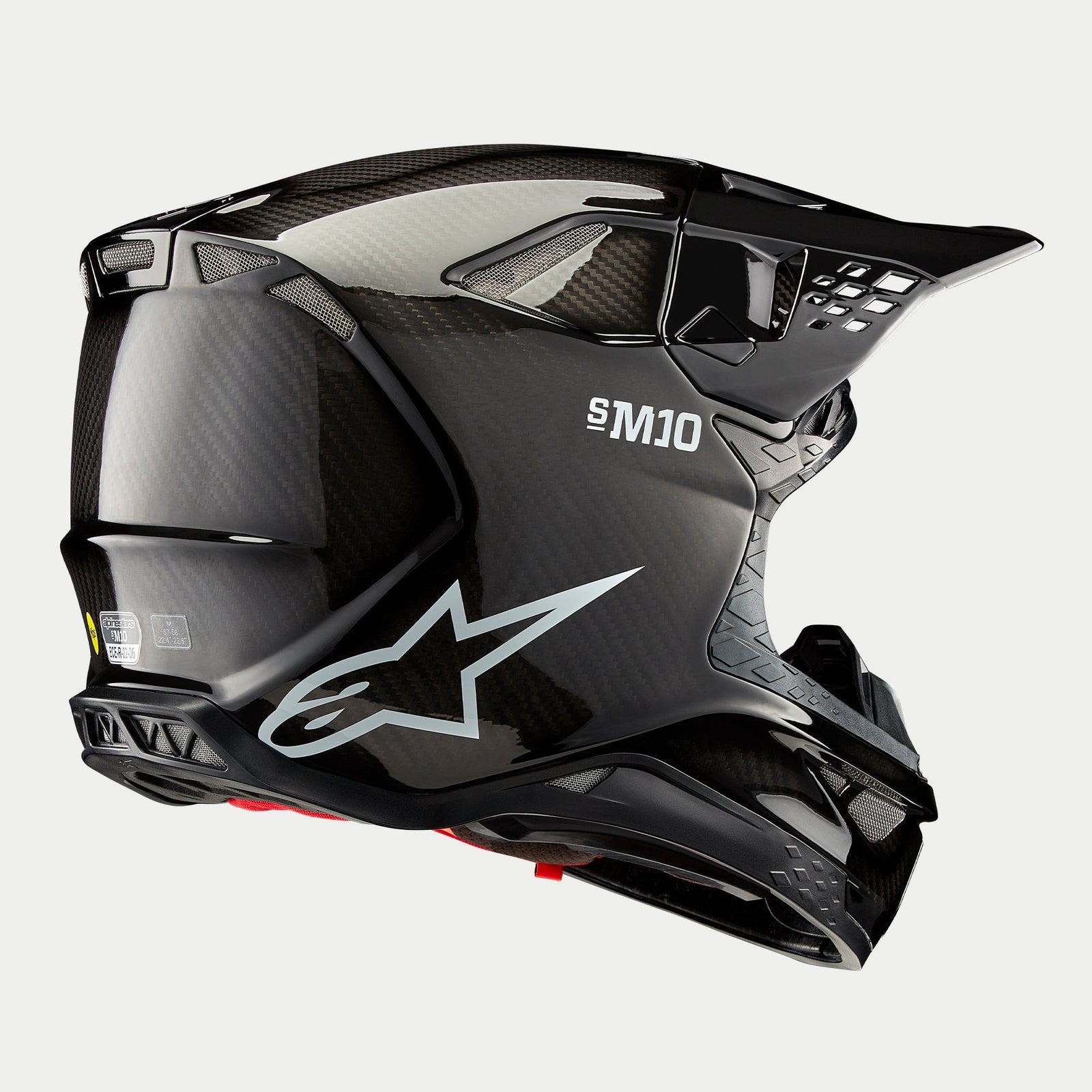 Kask Alpinestars Supertech M10 Solid, kask motocrossowy, wykończenie Black Glossy Carbon, białe logo Astars i branding S-M10, aerodynamiczna skorupa z widocznym splotem włókna węglowego i licznymi otworami wentylacyjnymi