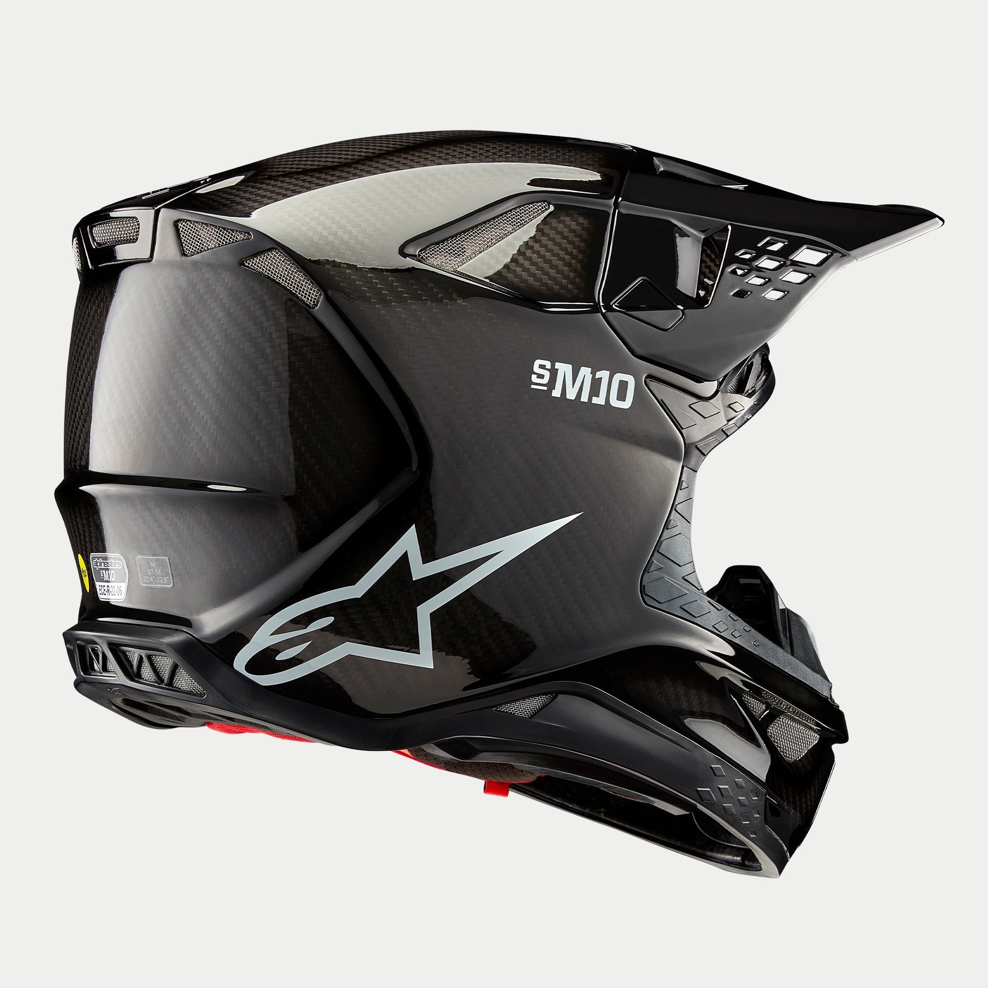 Kask Alpinestars Supertech M10 Solid, kask motocrossowy, wykończenie Black Glossy Carbon, białe logo Astars i branding S-M10, aerodynamiczna skorupa z widocznym splotem włókna węglowego i licznymi otworami wentylacyjnymi