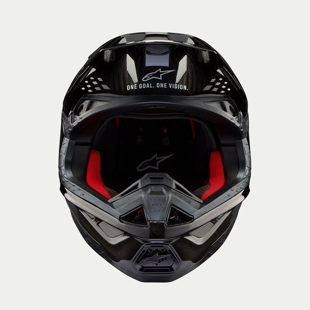 Kask Alpinestars Supertech M10 Solid, kask motocrossowy, czarny błyszczący karbon, widok z przodu ukazujący czerwoną wyściółkę wewnętrzną, skorupę z włókna węglowego oraz hasło „ONE GOAL. ONE VISION.” w obszarze daszka