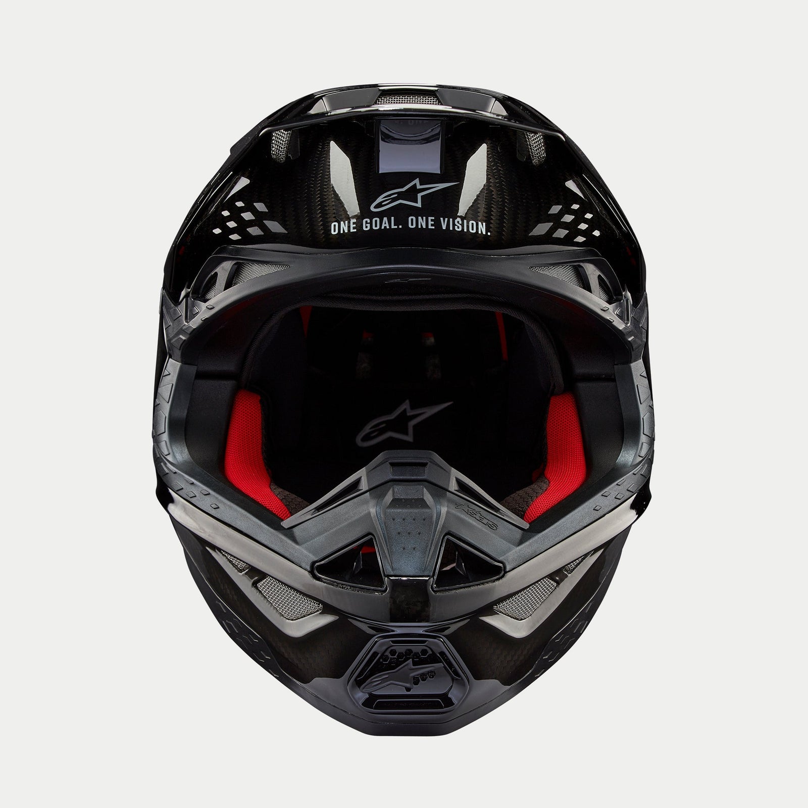 Kask Alpinestars Supertech M10 Solid, kask motocrossowy, czarny błyszczący karbon, widok z przodu ukazujący czerwoną wyściółkę wewnętrzną, skorupę z włókna węglowego oraz hasło „ONE GOAL. ONE VISION.” w obszarze daszka