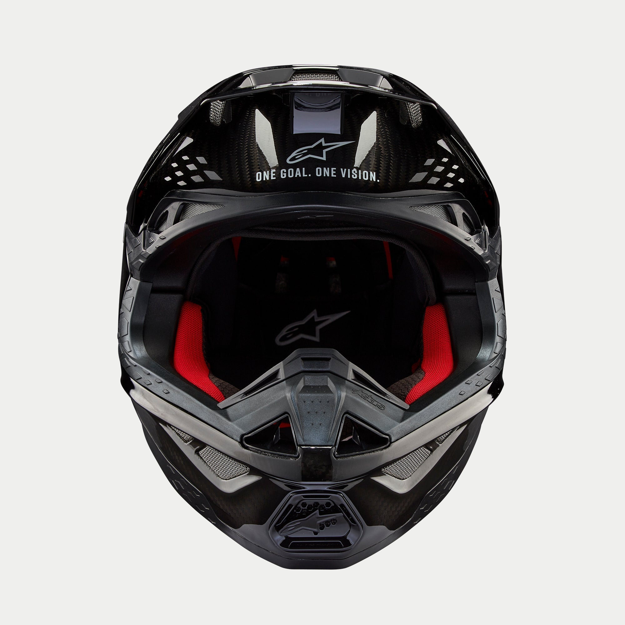 Kask Alpinestars Supertech M10 Solid, kask motocrossowy, czarny błyszczący karbon, widok z przodu ukazujący czerwoną wyściółkę wewnętrzną, skorupę z włókna węglowego oraz hasło „ONE GOAL. ONE VISION.” w obszarze daszka