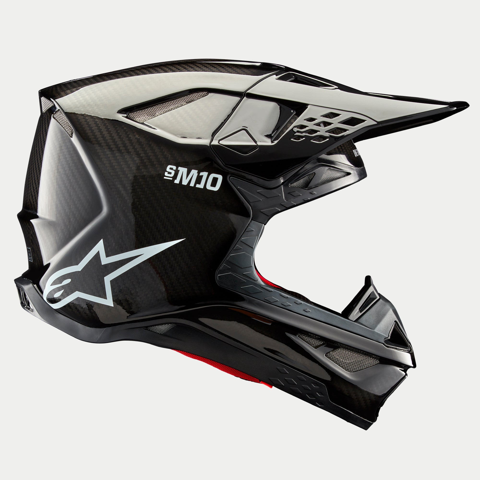 Kask Alpinestars Supertech M10 Solid, Black Glossy Carbon, kask motocrossowy, widok z profilu prezentujący splot błyszczącego włókna węglowego, oznaczenie S-M10, białe logo gwiazdy Alpinestars, aerodynamiczny design z daszkiem i otworami wentylacyjnymi