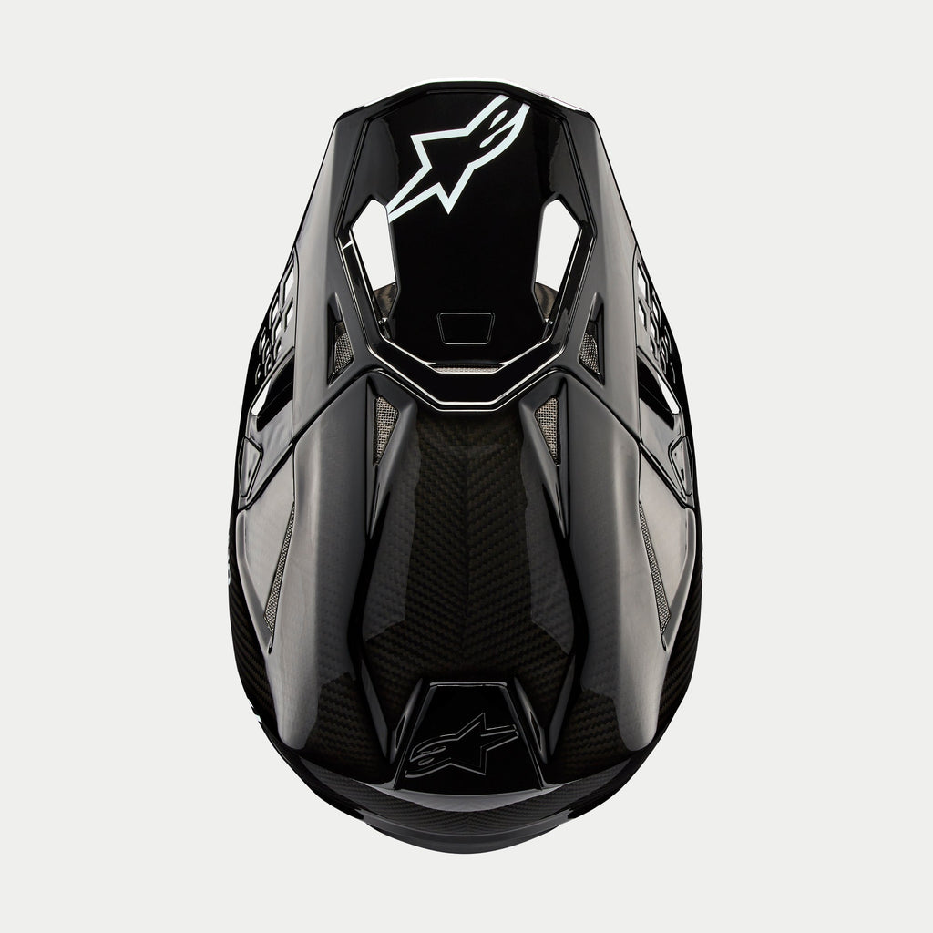 Alpinestars Supertech M10 Solid Helmet, kask motocrossowy, czarny błyszczący karbon, widok z góry ukazujący splot włókna węglowego, białe logo Astars na daszku, aerodynamiczny profil ze zintegrowanymi otworami wentylacyjnymi