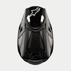 Alpinestars Supertech M10 Solid Helmet, kask motocrossowy, czarny błyszczący karbon, widok z góry ukazujący splot włókna węglowego, białe logo Astars na daszku, aerodynamiczny profil ze zintegrowanymi otworami wentylacyjnymi