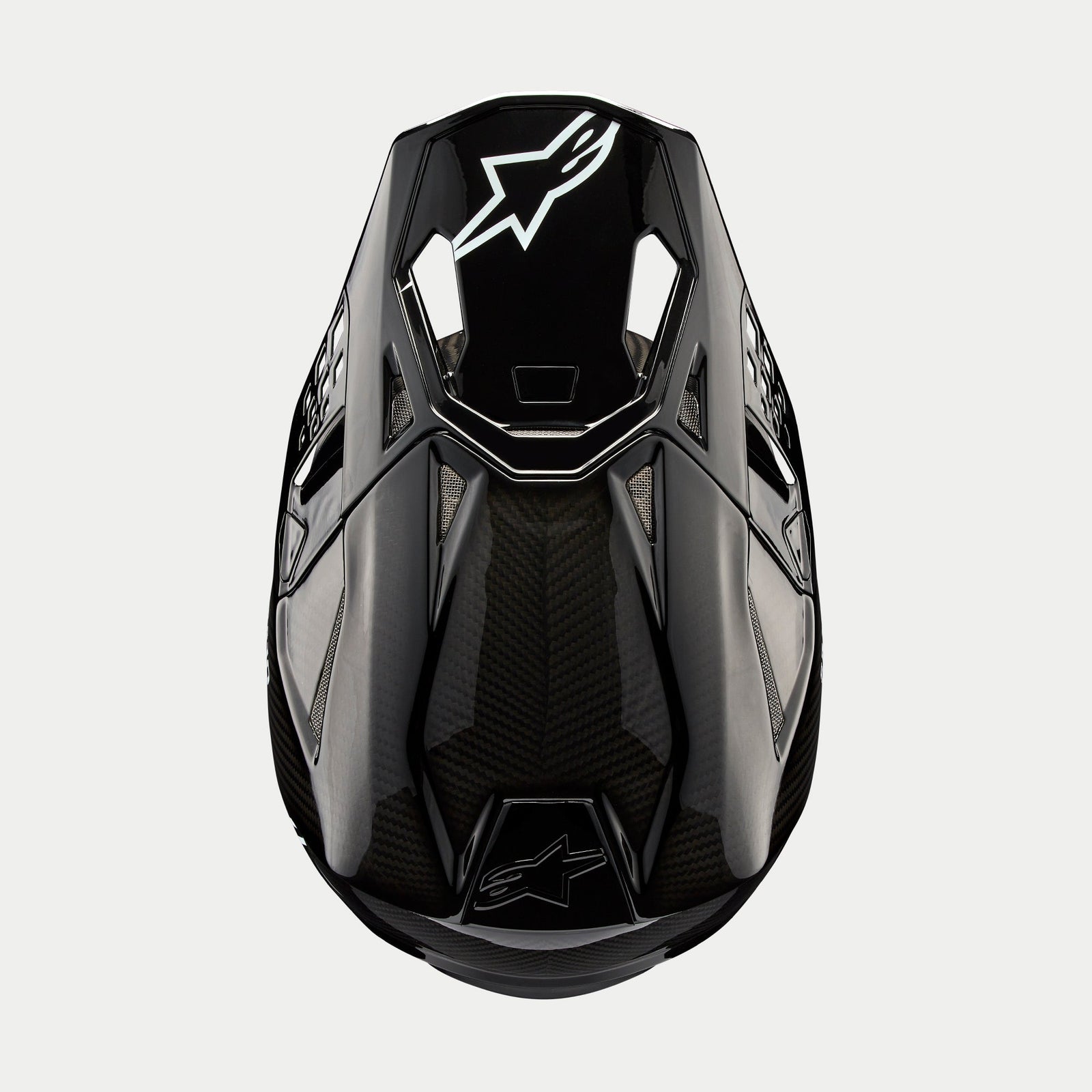 Alpinestars Supertech M10 Solid Helmet, kask motocrossowy, czarny błyszczący karbon, widok z góry ukazujący splot włókna węglowego, białe logo Astars na daszku, aerodynamiczny profil ze zintegrowanymi otworami wentylacyjnymi