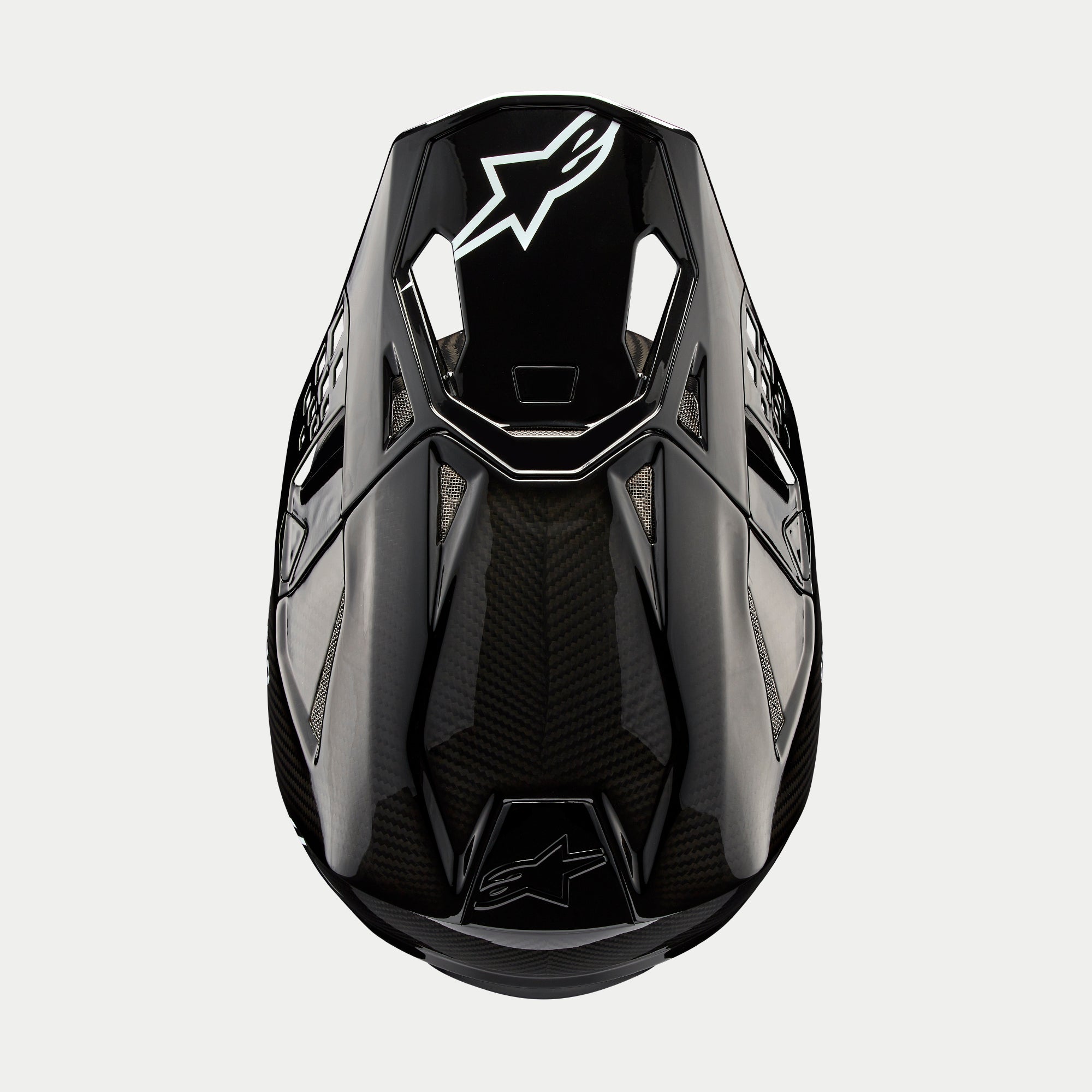 Alpinestars Supertech M10 Solid Helmet, kask motocrossowy, czarny błyszczący karbon, widok z góry ukazujący splot włókna węglowego, białe logo Astars na daszku, aerodynamiczny profil ze zintegrowanymi otworami wentylacyjnymi