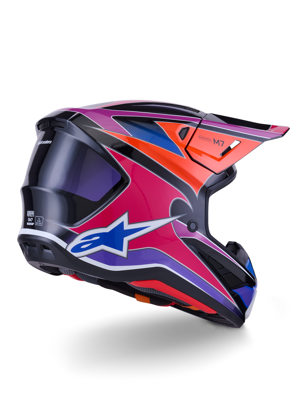 Kask Alpinestars S-M7 Fuse, kask motocrossowy, błyszczące wykończenie w kolorach niebieskim, fioletowym i różowym z pomarańczowymi i czarnymi akcentami, widok z tyłu pod kątem trzech czwartych ukazujący aerodynamiczną skorupę, daszek i otwory wentylacyjne, profesjonalna ochrona do wyścigów off-road