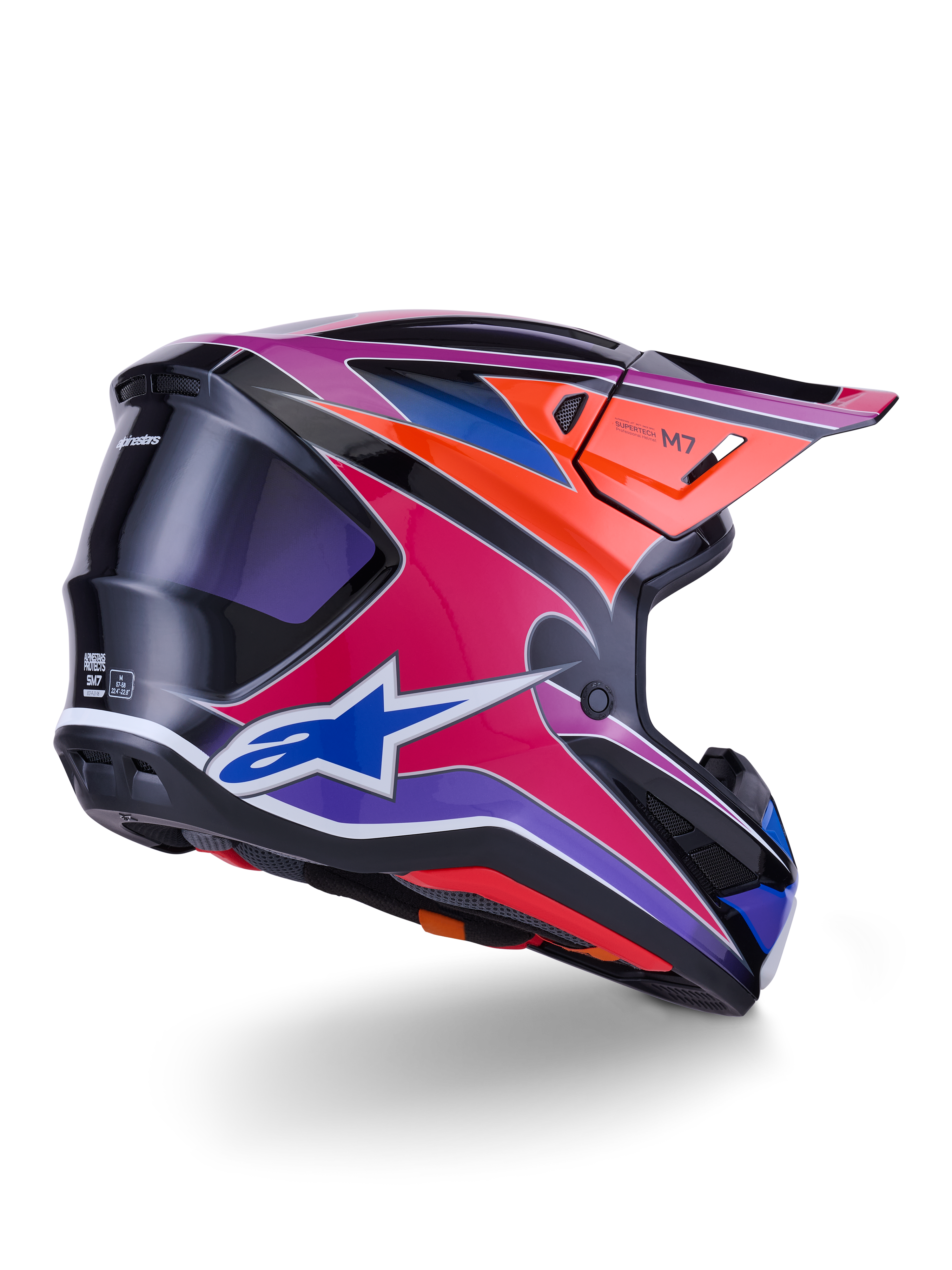 Kask Alpinestars S-M7 Fuse, kask motocrossowy, błyszczące wykończenie w kolorach niebieskim, fioletowym i różowym z pomarańczowymi i czarnymi akcentami, widok z tyłu pod kątem trzech czwartych ukazujący aerodynamiczną skorupę, daszek i otwory wentylacyjne, profesjonalna ochrona do wyścigów off-road