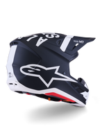Kask Alpinestars S-M7 Dasher, kask motocrossowy, matowy czarno-biały, widok z tyłu pod kątem trzech czwartych z dużym białym logo A-star z boku, wyraźnym białym brandingiem na górze, aerodynamiczną konstrukcją skorupy z widocznymi otworami wentylacyjnymi i czerwoną wyściółką.