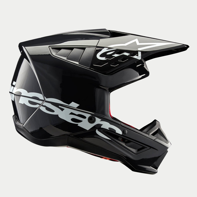 Alpinestars S-M5 Corp Helmet, kask motocrossowy, ciemnoszary błyszczący, widok z boku z dużym białym logo Alpinestars, białe logo gwiazdy na daszku, smukłe aerodynamiczne otwory wentylacyjne, błyszczące wykończenie, ochrona do wyścigów off-road