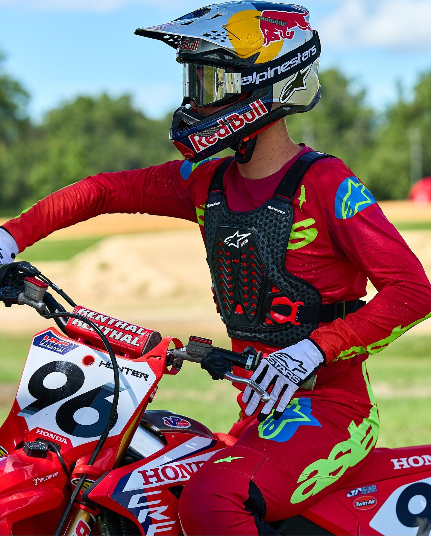 Motocross rider wearing Alpinestars A-5 Plasma Chest Protector in Black and Red, paired with a red and lime green racing jersey and pants, seated on a red Honda motorcycle, high-performance off-road protective gear