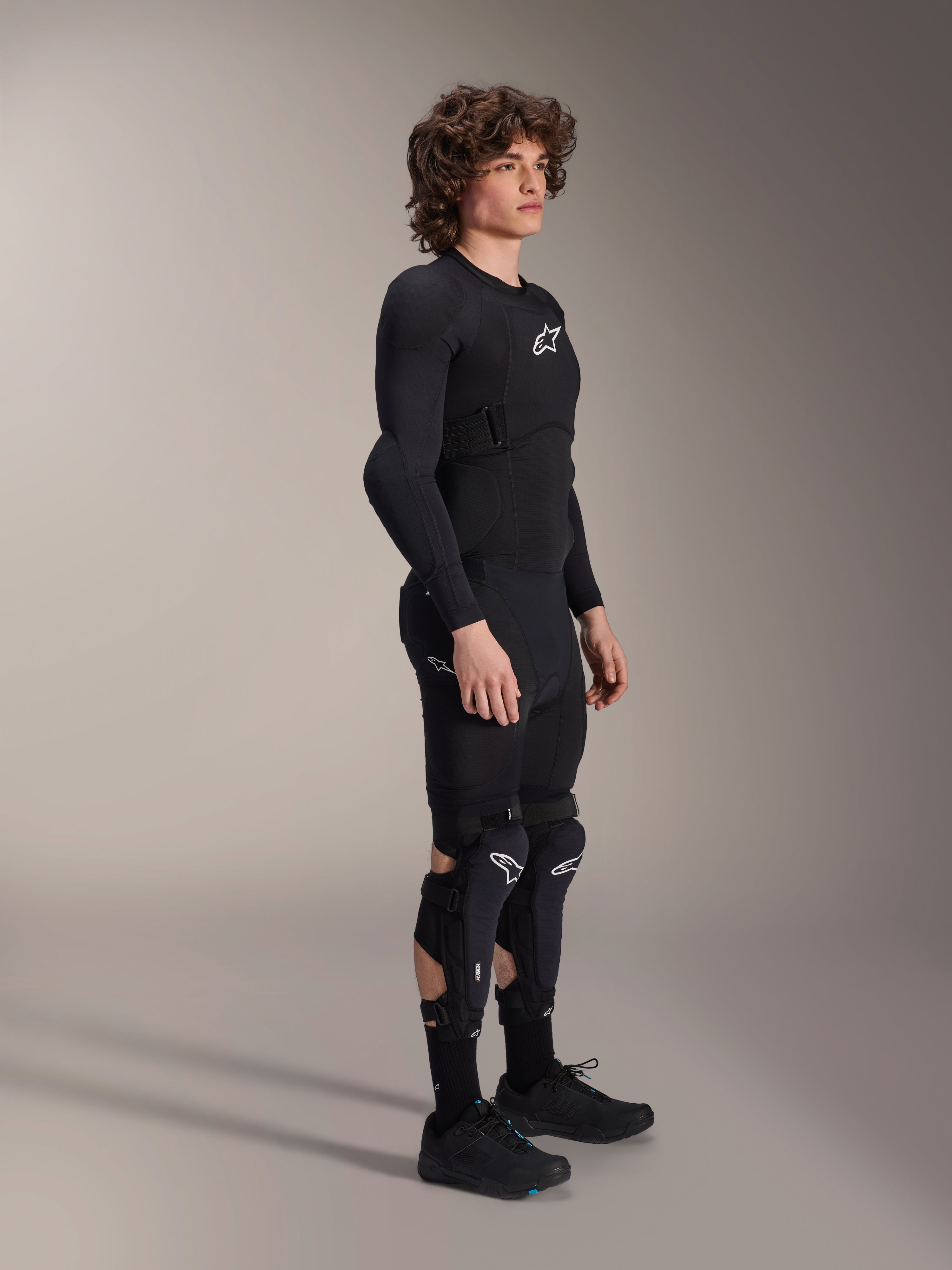 Kurtka ochronna Alpinestars A-Impact Plasma - Long Sleeve, czarna, prezentowana przez modela w dopasowanym zestawie z ochraniaczami kolan i szortami, białe logo Astars, oddychająca konstrukcja z siatki, opływowy design do jazdy terenowej.