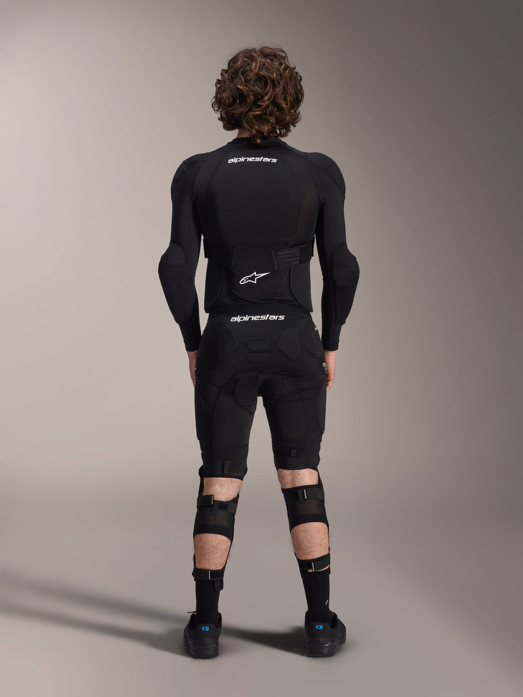 Kurtka ochronna Alpinestars A-Impact Plasma - długi rękaw, widok z tyłu, czarna z białymi logotypami Alpinestars, noszona ze spodenkami ochronnymi i ochraniaczami kolan dla pełnej ochrony MTB