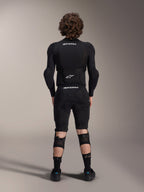 Kurtka ochronna Alpinestars A-Impact Plasma - długi rękaw, widok z tyłu, czarna z białymi logotypami Alpinestars, noszona ze spodenkami ochronnymi i ochraniaczami kolan dla pełnej ochrony MTB