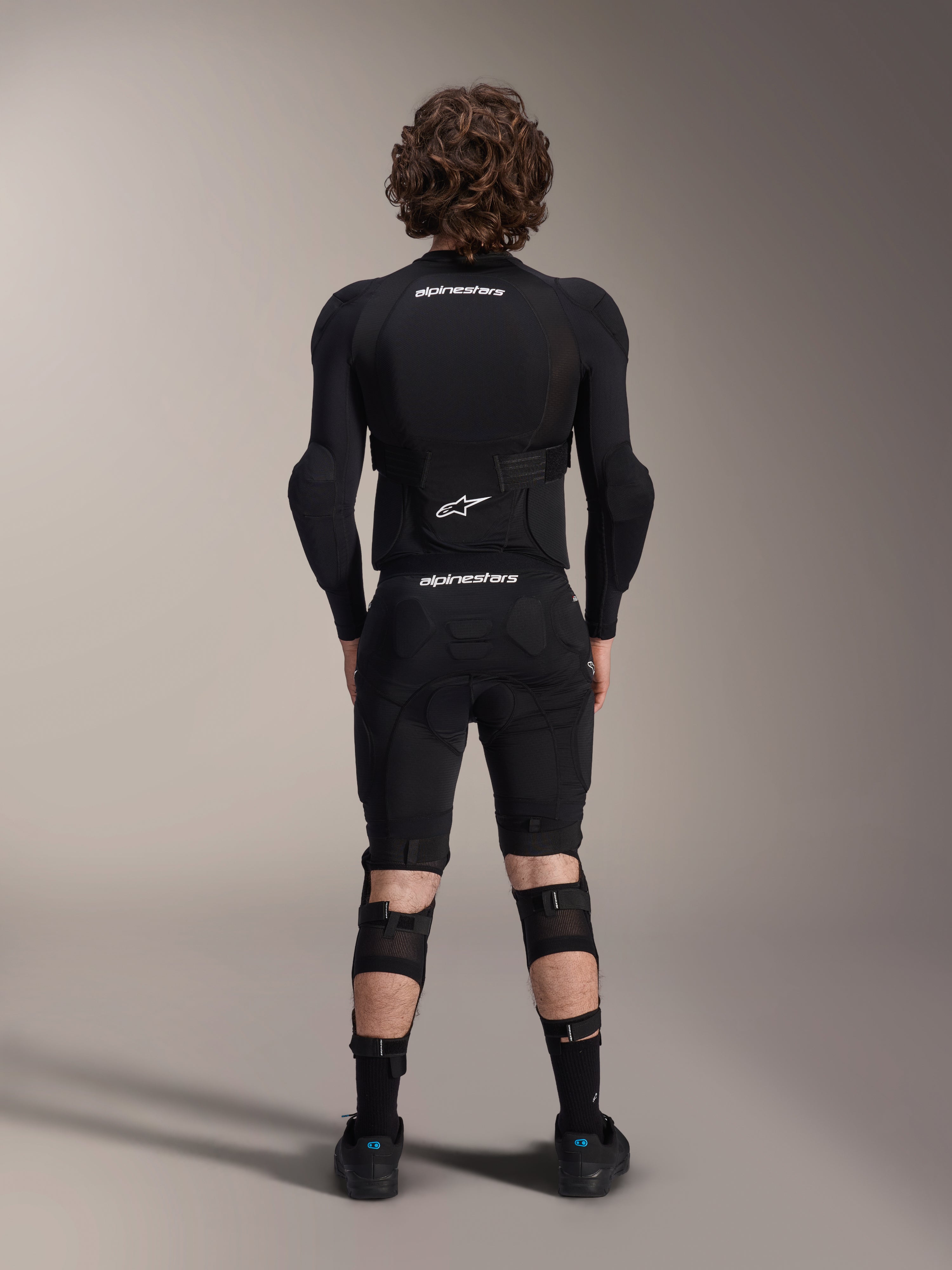 Kurtka ochronna Alpinestars A-Impact Plasma - długi rękaw, widok z tyłu, czarna z białymi logotypami Alpinestars, noszona ze spodenkami ochronnymi i ochraniaczami kolan dla pełnej ochrony MTB