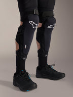 Ochraniacze kolan Alpinestars A-Impact Plasma Pro, czarno-białe, z brandingiem technologii Nucleon PLASMA, noszone z czarnymi skarpetami i czarnymi butami do rowerów górskich, bezpieczne paski na rzepy, ergonomiczny sprzęt ochronny do kolarstwa terenowego
