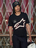 Koszulka Alpinestars Authority CSF, czarny T-shirt z krótkim rękawem, duże biało-czerwone konturowe logo Astars z grafiką „Alpinestars Protects”, ujęcie lifestyle z mężczyzną w czarnej czapce typu trucker trzymającym biały kask, casualowy streetwear motorsportowy