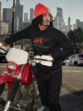 Alpinestars Pulse Hoodie, czarna polarowa bluza z kapturem z czerwono-szarym logo Astars Combo, mężczyzna w pomarańczowej czapce stojący obok czerwonego motocykla Honda w miejskiej scenerii, codzienna odzież motorsport streetwear