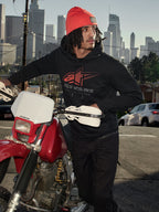 Alpinestars Pulse Hoodie, czarna polarowa bluza z kapturem z czerwono-szarym logo Astars Combo, mężczyzna w pomarańczowej czapce stojący obok czerwonego motocykla Honda w miejskiej scenerii, codzienna odzież motorsport streetwear