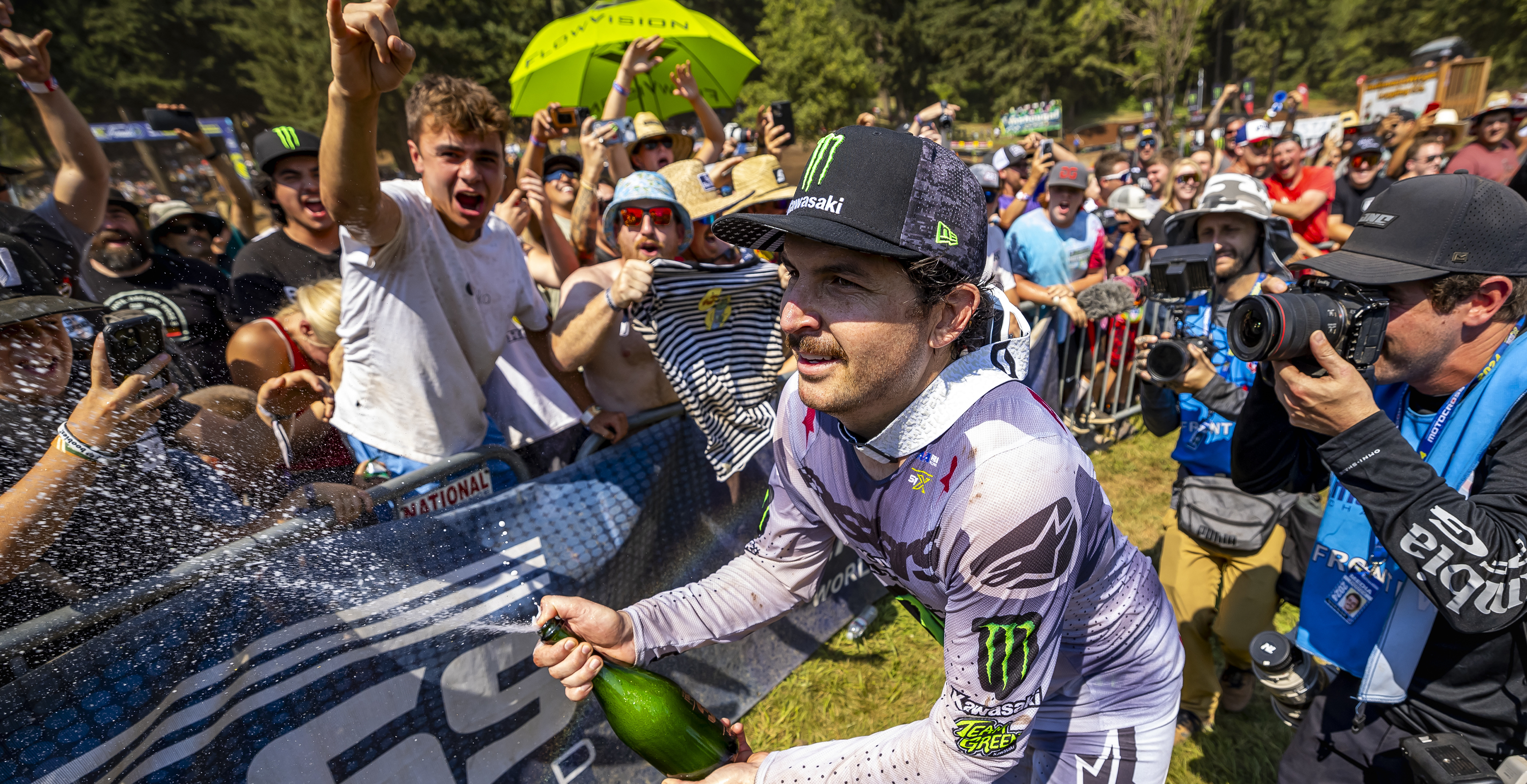 Jason Anderson wearing Alpinestars mx apparel celebrating with a bottle of champagne in front of a crowd after a motocross race.