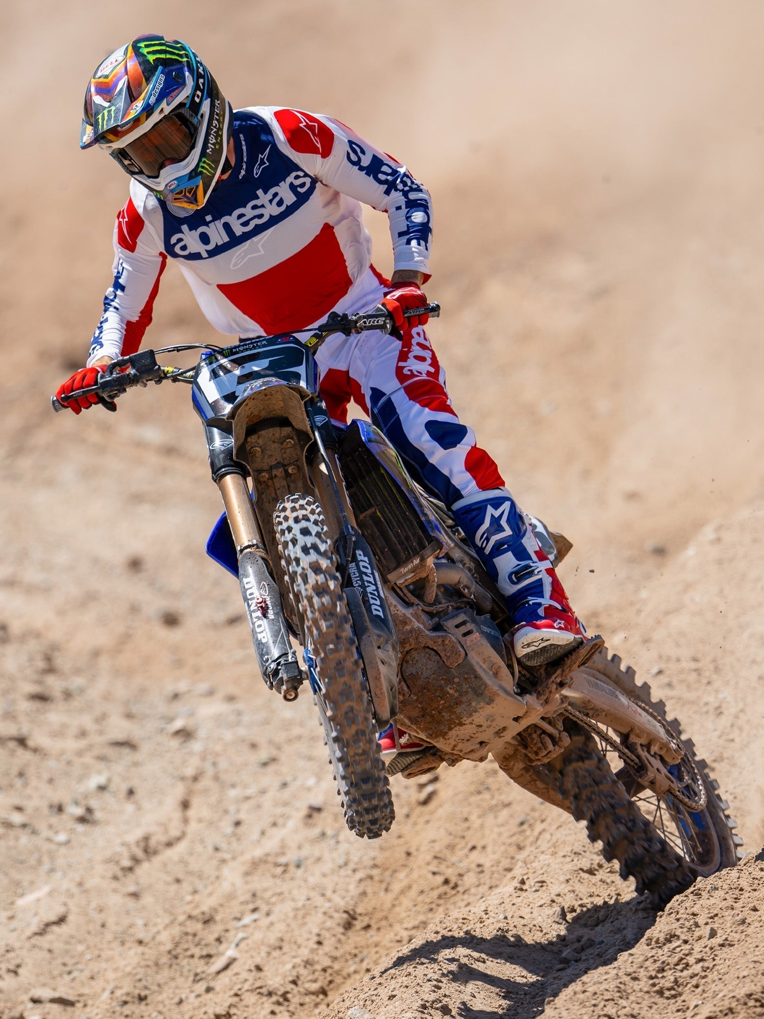 Motocross rider in action wearing Alpinestars Limited Edition Fortitude Tech 10 Boots, Bright Red White and Blue racing jersey and pants, coordinated patriotic gear set for off-road performance on a dirt track.