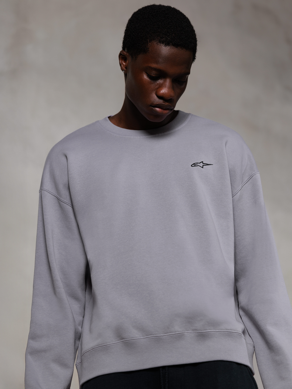 Alpinestars Essentials Ageless Crew, srebrna bluza typu crewneck klasy premium, z małym czarnym logo Alpinestars na piersi, prezentowana przez modela, casualowy styl streetwearowy z miękką teksturą polaru.