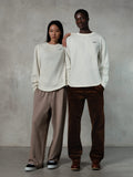 Alpinestars Essentials Ageless LS Tee, Long-Sleeve T-Shirt, Off White, worn by male and female models, small black Alpinestars logo on the chest, relaxed fit, styled with tan sweatpants and brown corduroy pants, casual motorsport-inspired streetwear