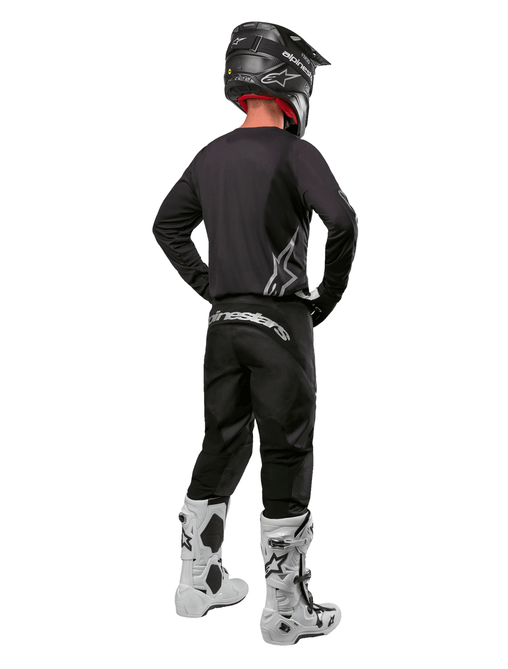 Alpinestars 2024 Fluid Graphite Gear Set, zawodnik motocrossowy widziany od tyłu, grafitowa koszulka i spodnie ze srebrnym brandingiem Alpinestars, czarny kask i białe buty motocrossowe, sportowy krój do jazdy terenowej