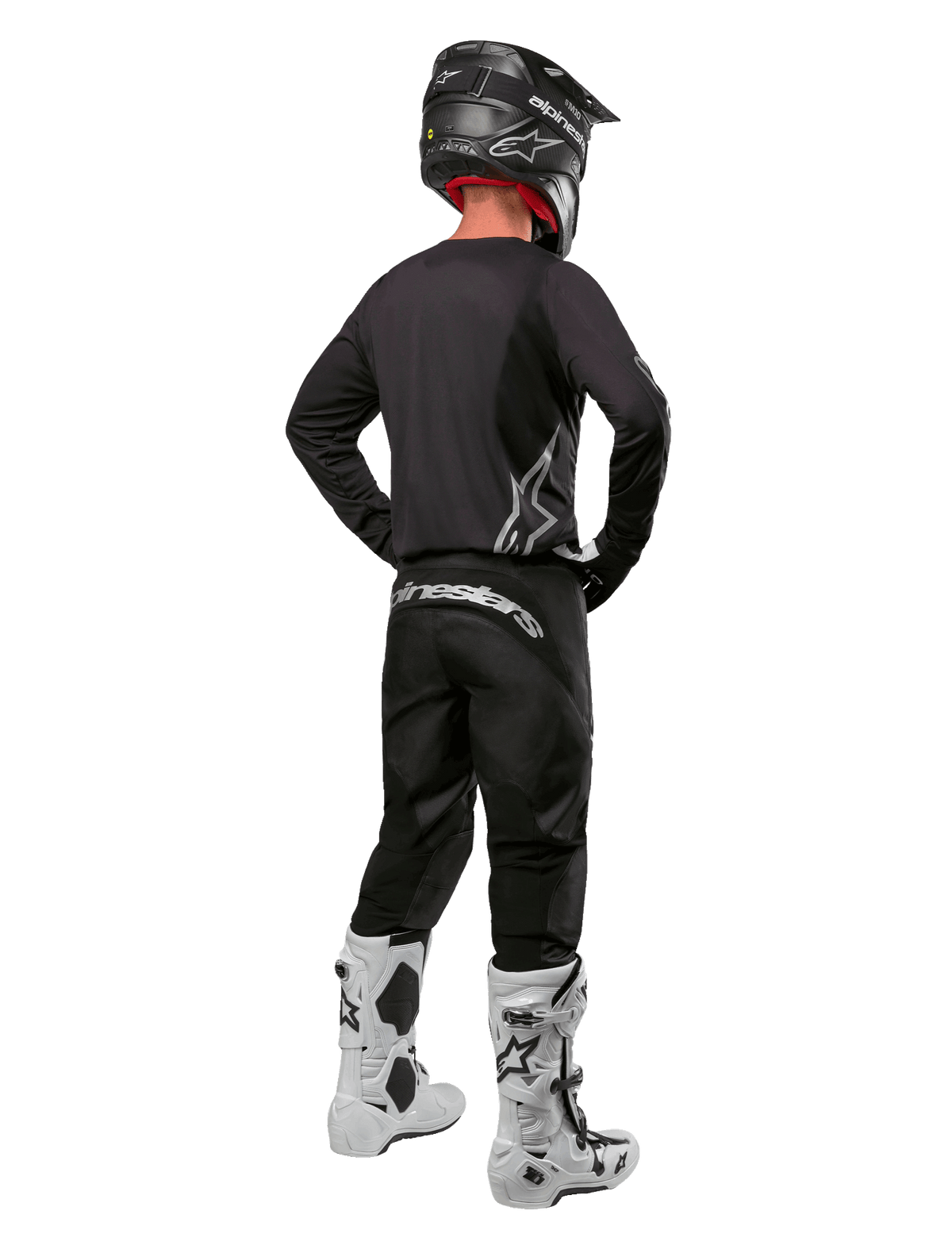 Alpinestars 2024 Fluid Graphite Gear Set, zawodnik motocrossowy widziany od tyłu, grafitowa koszulka i spodnie ze srebrnym brandingiem Alpinestars, czarny kask i białe buty motocrossowe, sportowy krój do jazdy terenowej