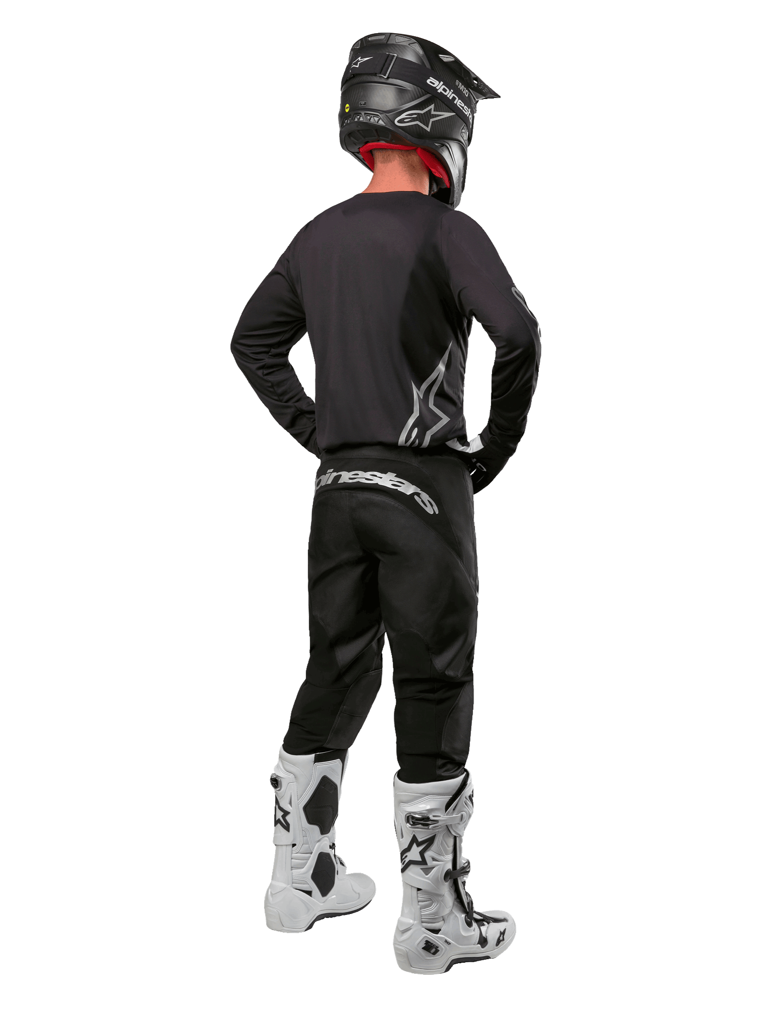 Alpinestars 2024 Fluid Graphite Gear Set, zawodnik motocrossowy widziany od tyłu, grafitowa koszulka i spodnie ze srebrnym brandingiem Alpinestars, czarny kask i białe buty motocrossowe, sportowy krój do jazdy terenowej