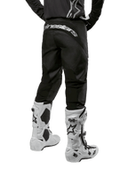 Zestaw Alpinestars 2024 Fluid Graphite, widok z tyłu czarno-szarych spodni motocrossowych z białym brandingiem Alpinestars na siedzeniu, biało-czarne buty motocrossowe, specjalistyczna odzież do wyścigów terenowych