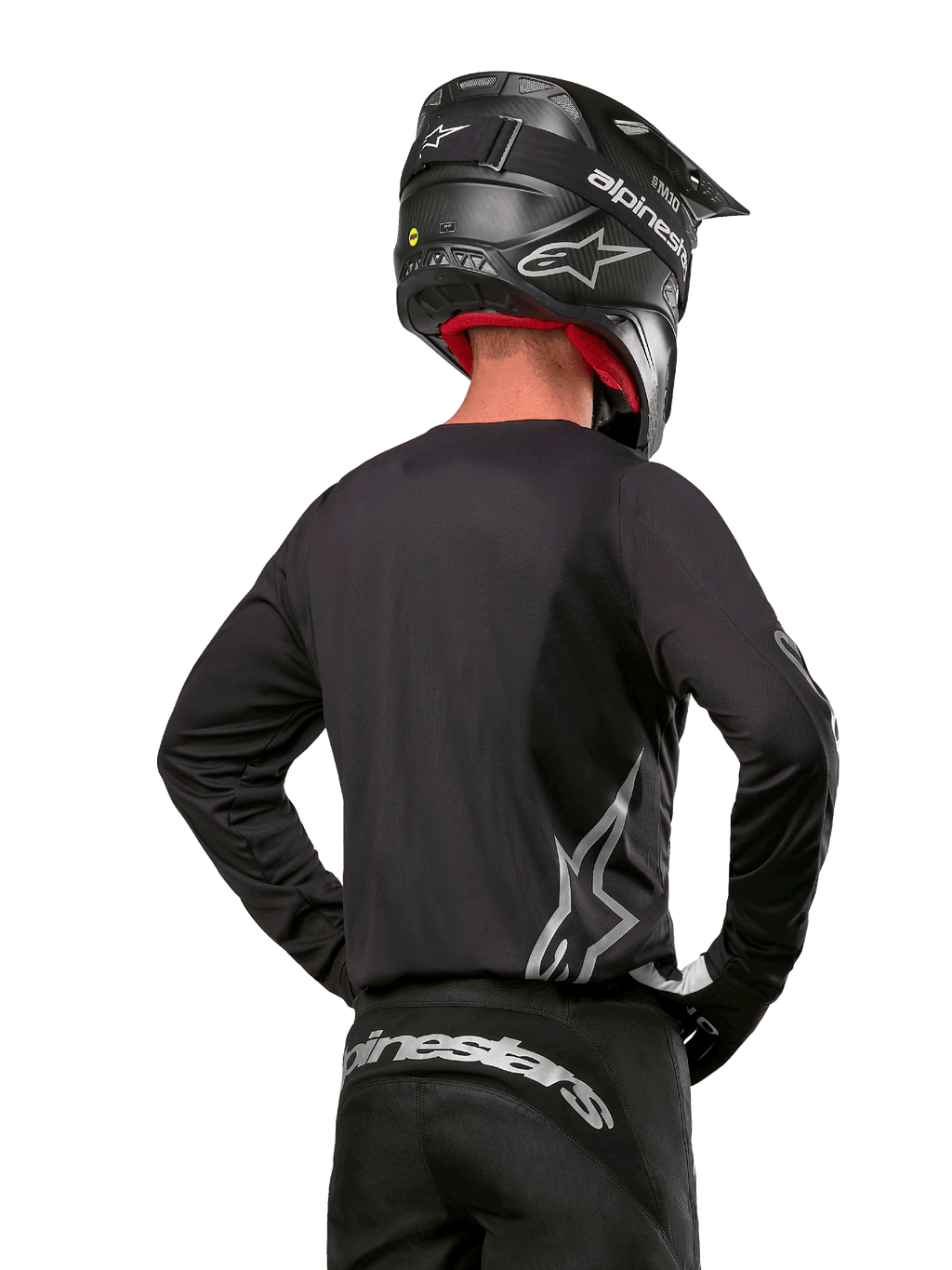 Alpinestars 2024 Fluid Graphite Gear Set, koszulka i spodnie motocrossowe, grafitowe i srebrne, widok z tyłu ze srebrnym brandingiem na dole pleców i w pasie, czarny kask z efektem karbonu, lekka poliestrowa konstrukcja do jazdy terenowej