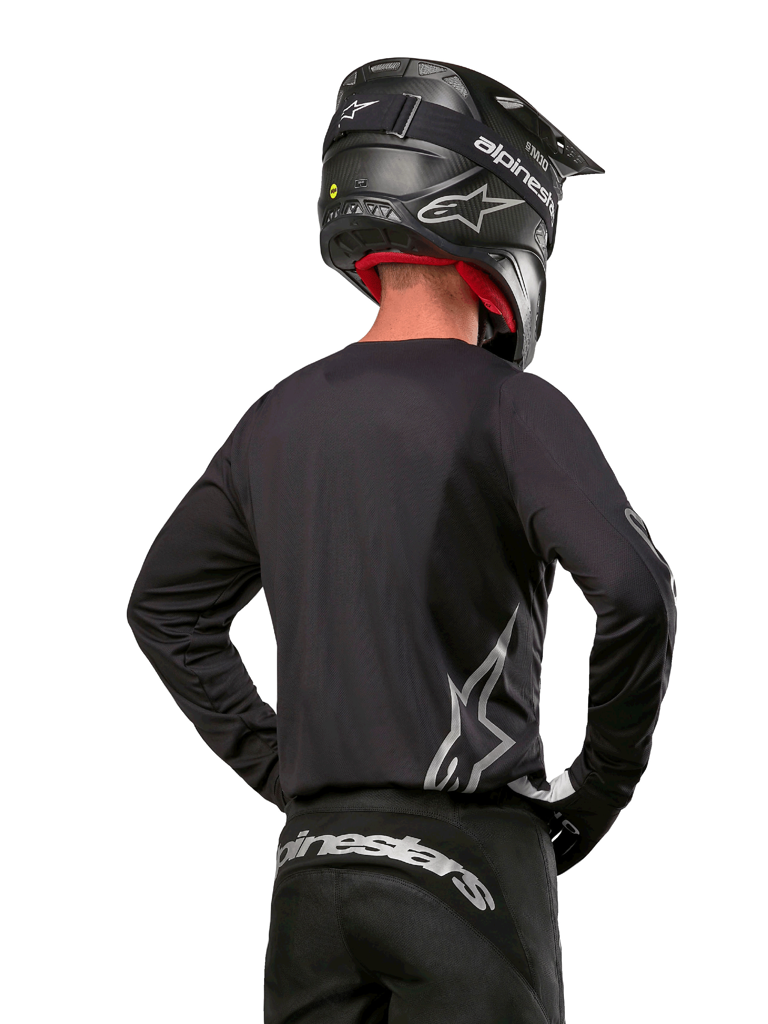 Alpinestars 2024 Fluid Graphite Gear Set, koszulka i spodnie motocrossowe, grafitowe i srebrne, widok z tyłu ze srebrnym brandingiem na dole pleców i w pasie, czarny kask z efektem karbonu, lekka poliestrowa konstrukcja do jazdy terenowej