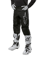 Alpinestars 2024 Fluid Graphite Pants, Motocross Pants, Black and Silver, featuring a silver Alpinestars logo on the thigh, shown worn with white motocross boots and gloves, designed for off-road motorcycle racing